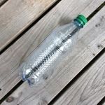 an empty plastic water bottle sitting on top of a wooden table next to a green cap