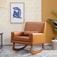 a brown leather rocking chair sitting in front of a wall with a painting on it