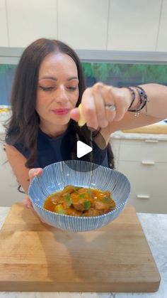 a woman in a blue shirt is eating food from a bowl on a cutting board