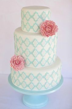 a three tiered cake with pink flowers on the top and blue trimmings