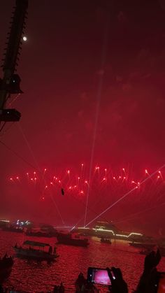 fireworks are lit up in the night sky above boats on water and people watching them