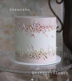 a white and pink cake with flowers on it is sitting on a glass platter