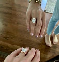 two people standing next to each other with their hands on the table and one is holding an engagement ring