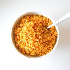 a white bowl filled with yellow food on top of a table next to a spoon