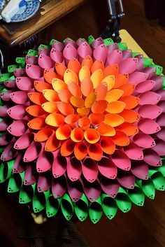 an orange and pink flower made out of plastic pipes on top of a wooden table