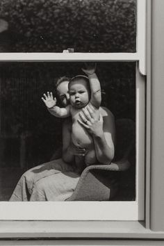 a woman holding a baby in her arms while sitting on a chair next to a window