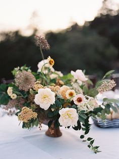 a vase filled with lots of flowers on top of a white table covered in greenery