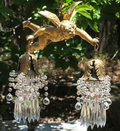 a pair of gold colored earrings with crystal beads hanging from it's sides, in front of some trees