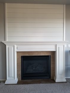 an empty living room with a fireplace and white paneling on the wall behind it