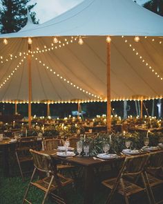 an outdoor tent with tables and chairs set up for dinner under string lights at night