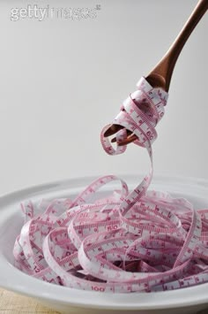 a white bowl filled with measuring tape and a wooden spoon sticking out of the top