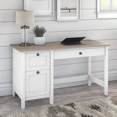 a white desk with two drawers and a laptop on it in front of three framed pictures