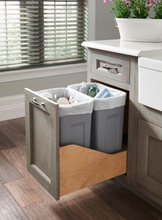 two trash cans are in the middle of a kitchen cabinet with drawers on both sides