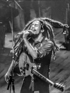 a man with dreadlocks on his head singing into a microphone and holding a guitar