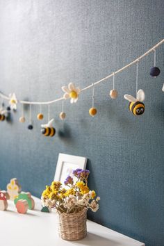 a basket with flowers and bees hanging from it on a string next to a blue wall