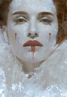 a woman with blood on her face and white fur around her neck, wearing red lipstick