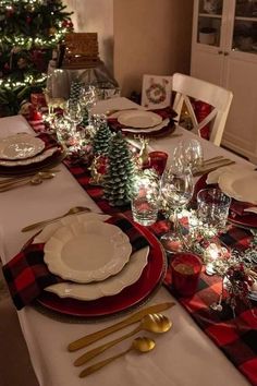 a dining room table set for christmas with plates, silverware and candlesticks