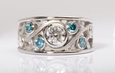 a white gold ring with blue topaz and diamonds on the sides, sitting on a reflective surface