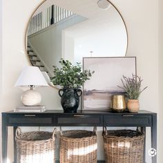 two wicker baskets under a mirror on top of a black table with a lamp