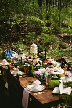 a table set up in the woods with flowers and plates on it for a tea party