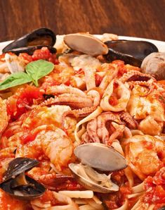 a plate of pasta with shrimp, clams and sauce on it sitting on a wooden table