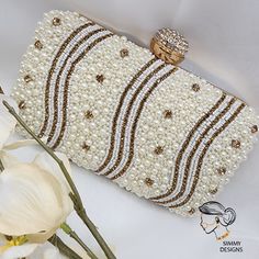 a white purse with pearls and diamonds on the front, sitting next to some flowers