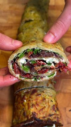 a person holding a sandwich in their hand on top of a wooden table next to a burrito