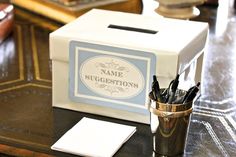 a box with some pens in it on a table next to a cup and napkins