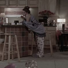 a woman standing at the counter in a kitchen next to stools and a table