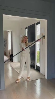 a woman in white is holding a large stick and standing on the floor with her hands behind her back