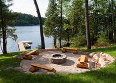 a fire pit with benches around it in the grass next to a body of water