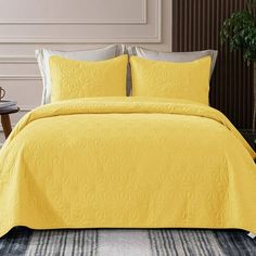 a bed with yellow comforter and pillows in a room next to a plant on the floor