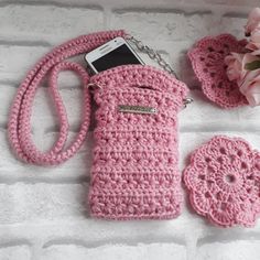 a pink crocheted cell phone case next to a flower and two small purses