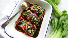 a white plate topped with meat covered in sauce and green onions next to a spoon