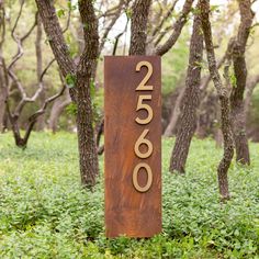 a wooden sign sitting in the middle of a lush green field next to some trees