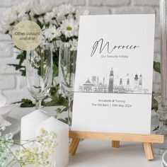 a table set up with wine glasses, flowers and an easel on the table