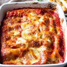 a casserole dish with cheese and sauce in it on a table next to bread