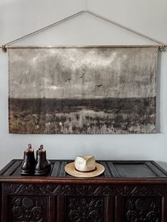 a painting hanging on the wall above a table with a hat and two beer bottles