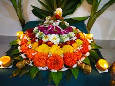 an arrangement of flowers and candles on a blue table cloth with green leaves around it