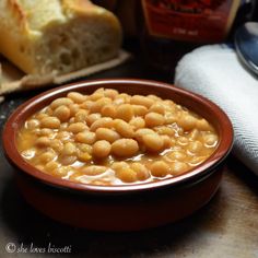 a brown bowl filled with beans next to bread