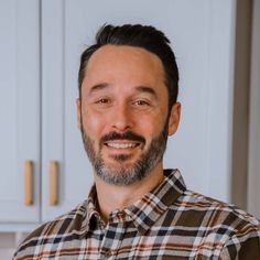 a man with a goatee smiles at the camera in front of white cupboards