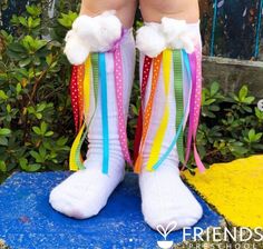 a child's legs with colorful socks and rainbow ribbons on them, standing in front of bushes