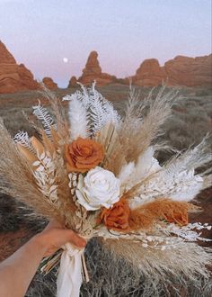 a person holding a bouquet with flowers in the middle of desert land at sunset or dawn