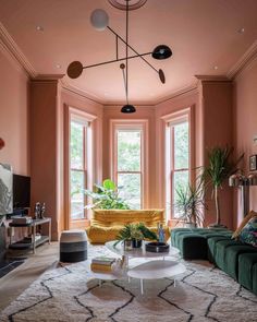 a living room with pink walls and green couches in front of two large windows