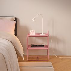 a pink shelf next to a bed with a white lamp on it and a rug