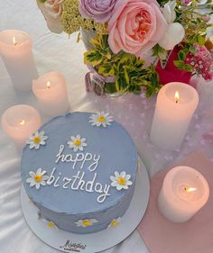 a birthday cake sitting on top of a table next to some candles and pink flowers