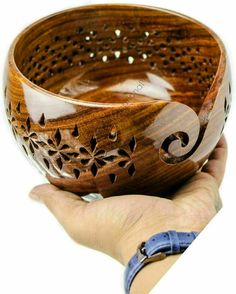 a hand holding a wooden bowl with holes in the middle and filigrees on it