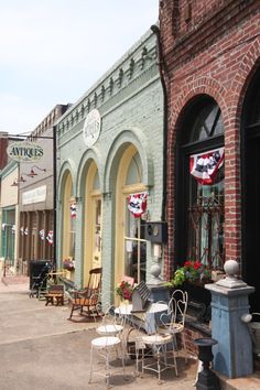 an old brick building with several chairs and tables outside on the sidewalk in front of it