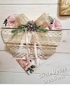 a heart shaped box with lace and flowers on it sitting on a white wooden surface