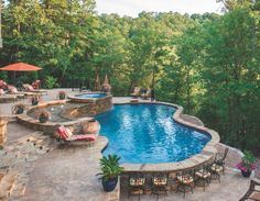 an outdoor swimming pool surrounded by patio furniture and umbrellas with trees in the background